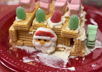 Wafer cookie house decorated with candies on a red plate.
