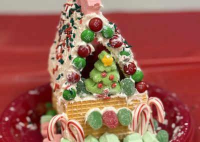 Gingerbread house made of wafers, icing, and candies on a red plate.