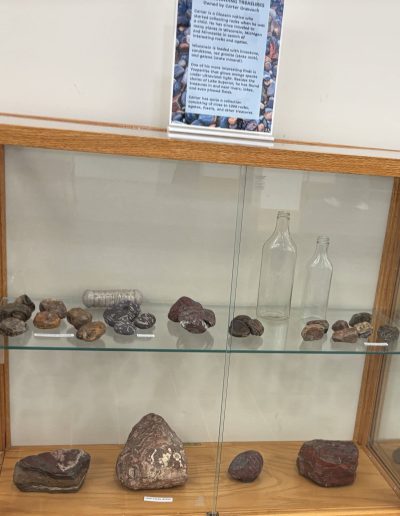 Display of various labeled stones and minerals in a glass cabinet.